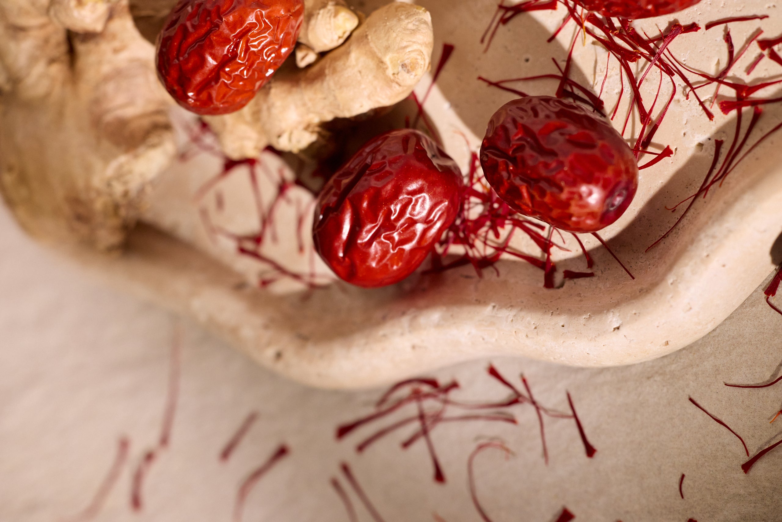 Dried red dates with saffron threads and ginger root on ceramic surface.